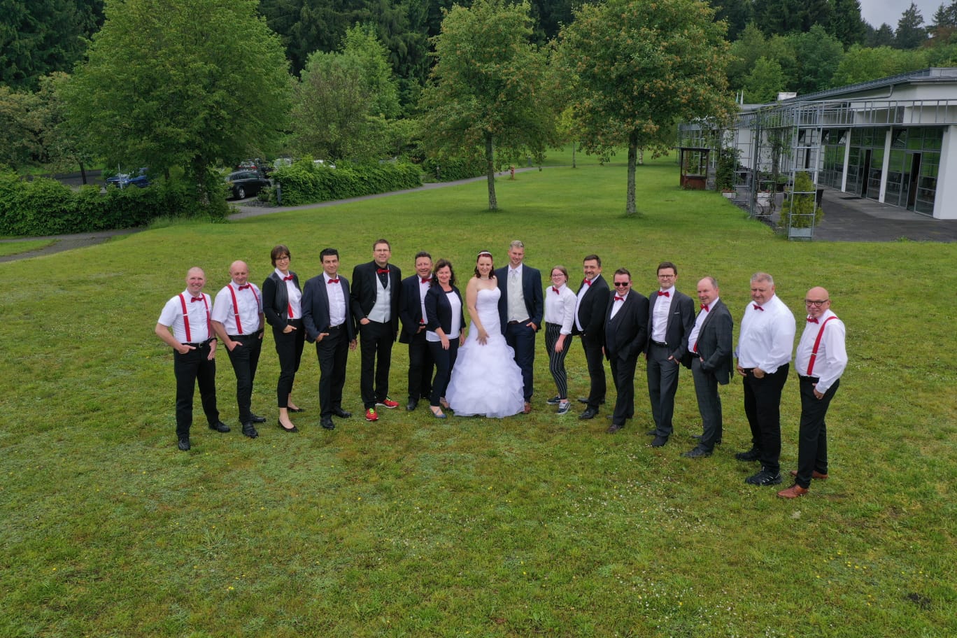 Die HochzeitsDJ mit der Roten Fliege stehehn zusammen mit einem Brautpaar auf der Wiese