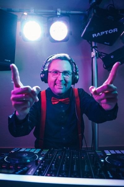 HochzeitsDJ Michael in Franken und Region Schweinfurt und Würzburg, stilecht - Kopfhörer, Fliege, rote Hosenträger - mit einem energischen Lächeln hinter dem Mischpult und bunten Lichtern nach oben.